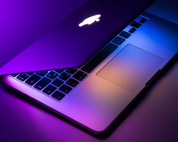 Silver MacBook laptop with glowing Apple logo in purple light.